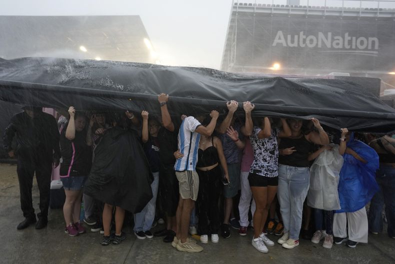 Aficionados se cubren de un aguacero mientras esperan ingresar al estadio DRV Pink, sede del Inter Miami, para la presentación de Lionel Messi, el domingo 16 de julio de 2023, en Fort Lauderdale, Florida. (AP Foto/Rebecca Blackwell)