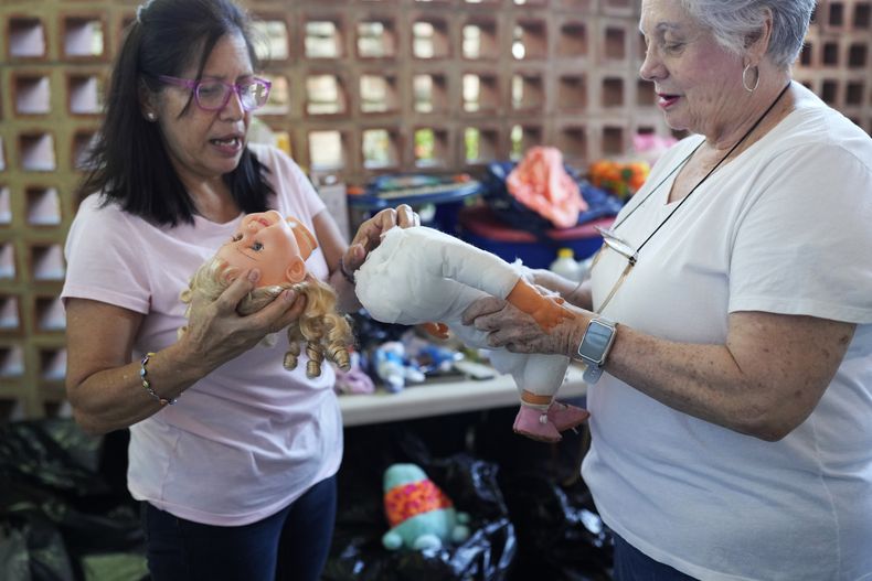 Las voluntarias Aides Jiménez, a la izquierda, y Miriam Goodman debate sobre la mejor manera de recuperar una muñeca usada, en la organización sin fines de lucro Hospital de los Peluches, en Caracas, Venezuela, el jueves 5 de diciembre de 2024. (AP Foto/Ariana Cubillos)