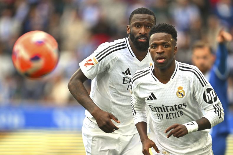 Vinicius Junior, a la derecha, del Real Madrid, y Antonio Rudiger persiguen el balón durante un partido de fútbol de La Liga española entre el Alavés y el Real Madrid en el estadio Mendizorroza en Vitoria, España, el domingo 13 de abril de 2025. (AP Foto/Miguel Oses)