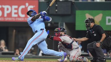 Adolis García, izquierda, de los Rangers de Texas, hace seguimiendo después de conectar un cuadrangular solitario frente a los Medias Rojas de Boston, ante las miradas del receptor Connor Wong, centro, y el umpire principal Néstor Ceja, derecha, durante la sexta entrada del juego de béisbol de las mayores, el domingo 30 de marzo de 2025, en Arlington, Texas. (AP Foto/LM Otero)