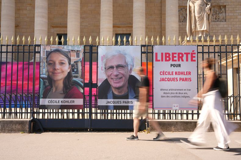 ARCHIVO - La gente pasa junto a los retratos de los franceses Cécile Kohler y Jacques Paris, quienes estuvieron presos en Irán, frente a la Asamblea Nacional Francesa, en París el 3 de julio de 2025. (Foto AP/Aurelien Morissard, Archivo)