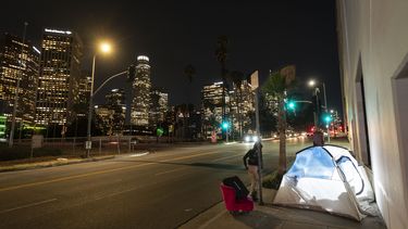 ARCHIVO - En esta imagen, iluminada por un flash externo, una mujer pasa por delante de una tienda de campaña de una persona sin hogar con una silla, en el centro de Los Ángeles, el 16 de febrero de 2023. (AP Foto/Jae C. Hong, archivo)