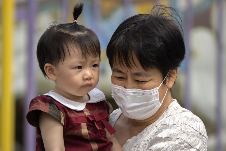 En esta imagen de archivo, una mujer con mascarilla lleva una niña en brazos en un parque público en Beijing, el 1 de junio de 2023. (AP Foto/Mark Schiefelbein, archivo)