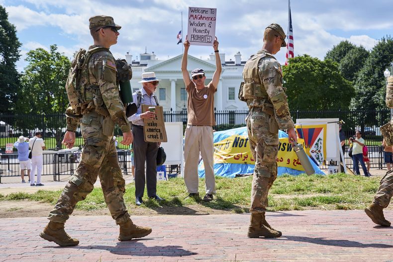 Miembros de la Guardia Nacional patrullan Lafayette Park cerca de la Casa Blanca, el viernes 29 de agosto de 2025, en Washington, mientras que el manifestante Will Roosien, de Grand Rapids, Michigan, que pretende inspirar a otras personas de su generación para que protesten, sostiene un cartel sobre el movimiento MAGA. (AP Foto/Jacquelyn Martin)