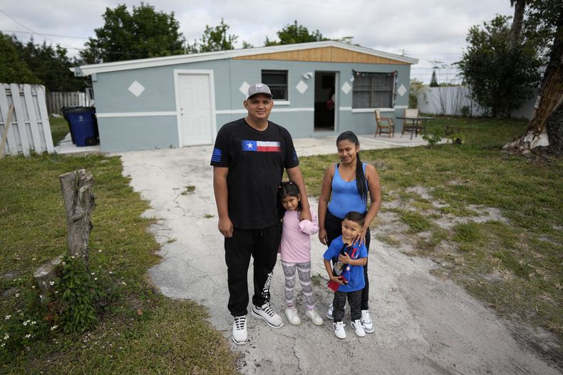Alexis Llanos, a la izquierda, su pareja Diomaris Barboza, y sus hijos Alexa, de 7 años, y Alexis, de 3, posan el 27 de diciembre de 2023 para una foto afuera de la casa de Lehigh Acres, Florida, a la que se mudaron en octubre de 2023, cinco años después de haber salido de Venezuela hacia Colombia por amenazas de muerte. La de Llanos es una de las primeras familias de migrantes que llegaron a Estados Unidos legalmente bajo un nuevo programa conocido como Oficinas de Movilidad Segura, que busca agilizar el proceso de refugiados. (AP Foto/Rebecca Blackwell)