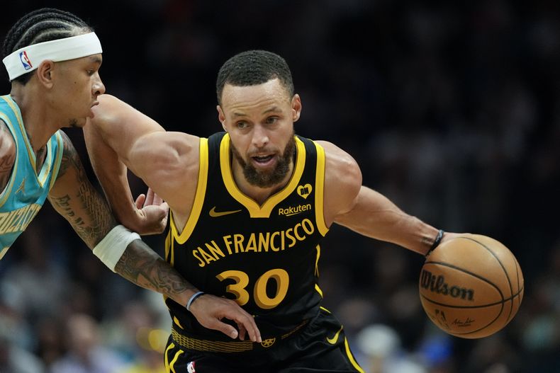 Stephen Curry, de los Warriors de Golden State, conduce el balón hacia la canasta pasando al lado de Tre Mann, de los Hornets de Charlotte, durante la primera mitad del juego de baloncesto de la NBA, el viernes 29 de marzo de 2024, en Charlotte, Carolina del Norte. (AP Foto/Chris Carlson)