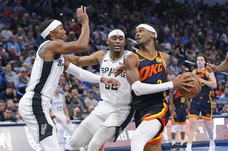 Shai Gilgeous-Alexander, base del Thunder de Oklahoma City, avanza a la cesta frente a Devonte Graham y Malaki Branham, de los Spurs de San Antonio, en el partido del martes 14 de noviembre de 2023 (AP Foto/Nate Billings)
