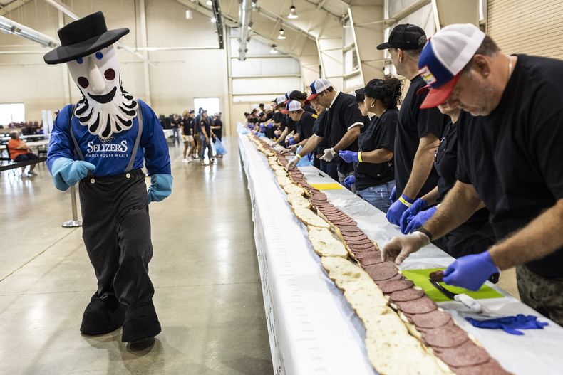 La mascota de Seltzer observa cómo voluntarios ensamblan un sándwich de mortadela de 45,7 metros (150 pies) de largo en Lebanon, Pensilvania, el 25 d ejulio de 2023. (Sean Simmers/The Patriot-News vía AP)