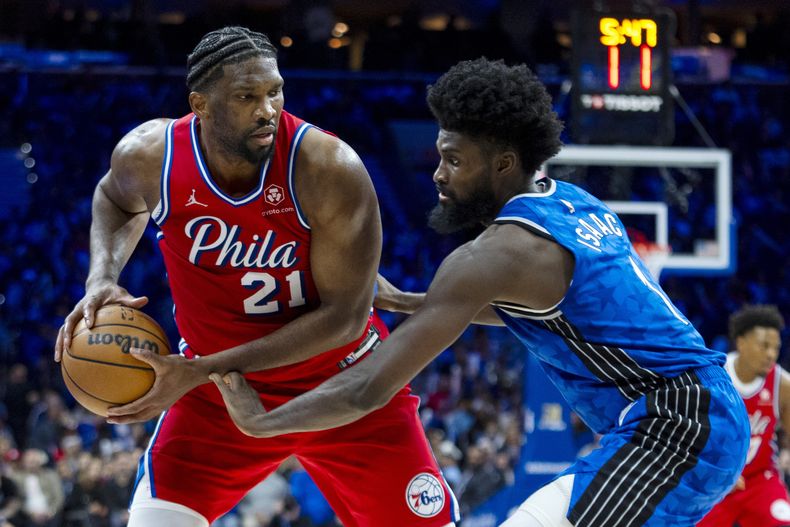 Joel Embiid de los 76ers de Filadelfia (izquierda) intenta hacer un movimiento ante Jonathan Isaac del Magic de Orlando, durante la segunda mitad del juego de baloncesto de la NBA, el viernes 12 de abril de 2024, en Filadelfia. (AP Foto/Chris Szagola)