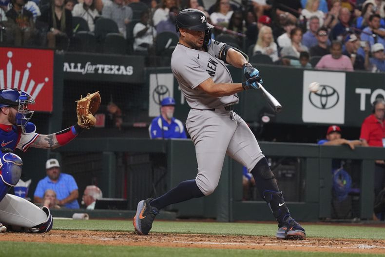 Giancarlo Stanton, derecha, de los Yankees de Nueva York, batea un jonrón en el que remolcó a Paul Goldschmidt ante la mirada de Jonah Heim, izquierda, receptor de los Rangers de Texas, durante la cuarta entrada del juego de béisbol de Grandes Ligas, el lunes 4 de agosto de 2025, en Arlington, Texas. (AP Foto/LM Otero)
