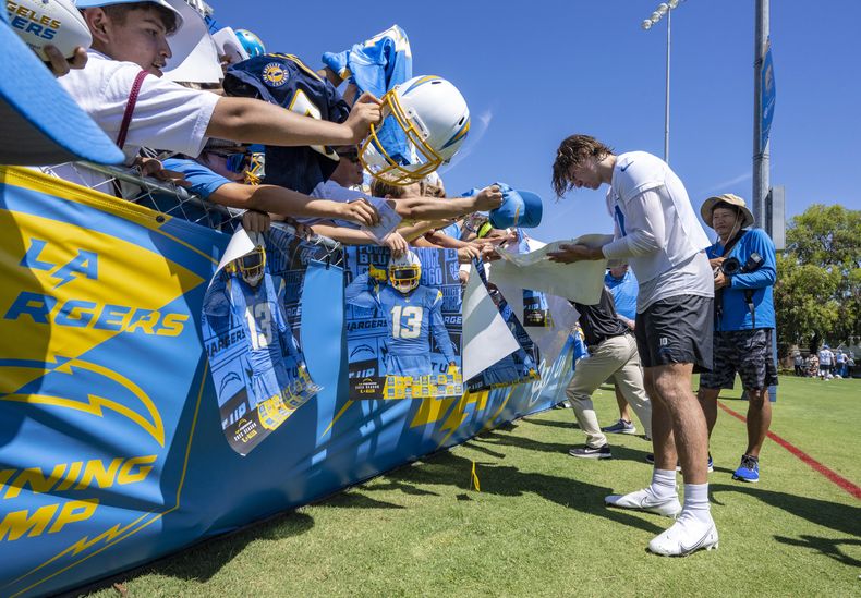 Justin Herbert, derecha, quarterback de los Chargers de Los Ángeles, firma autógrafos para los fanáticos después del primer entrenamiento del campamento de prácticas del equipo en Costa Mesa, California, el miércoles 26 de julio de 2023. (Mark Rightmire/The Orange County Register vía AP)