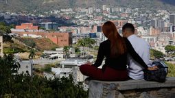 Una pareja sentada en un banco en un mirador con vistas a la embajada de Estados Unidos, en el centro a la izquierda, en Caracas, Venezuela, el viernes 9 de enero de 2026. (AP Foto/Cristian Hernández)