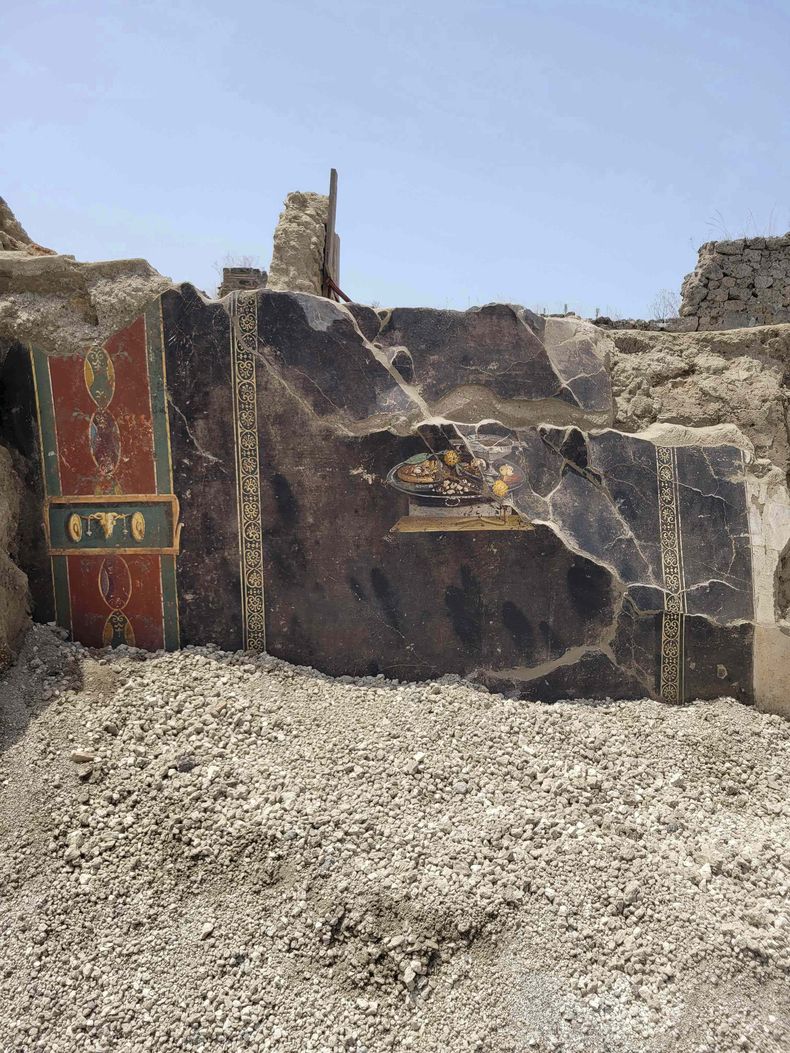 Esta imagen proporcionada el martes 27 de junio de 2023 por el Sitio Arqueológico de Pompeya muestra una pared de una antigua casa pompeyana con frescos incluyendo uno que representa una mesa con comida. El fresco fue encontrado en el atrio de una casa en Insula 10 de Regio IX en una excavación, a la que se anexó una panadería, ya explorada parcialmente entre 1888 y 1891 y cuyas investigaciones se reanudaron en enero pasado.(Sitio Arqueológico de Pompeya vía AP, ho)