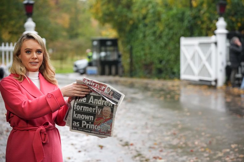 Una presentadora de televisión sostiene un periódico con una foto del príncipe Andrés mientras habla a la cámara en una puerta cerca del Royal Lodge, tras el anuncio de que a Andrés se le retirarán sus títulos nobiliarios y abandonará la mansión de 30 habitaciones que ha ocupado durante más de 20 años en Windsor, Inglaterra, el viernes 31 de octubre de 2025. (Foto AP/Alastair Grant)