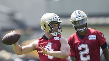Derek Carr, quarterback de los Saints de Nueva Orleans, lanza el balón mientras que Jameis Winston (2) observa durante un entrenamiento de la NFL, en Metairie, Louissiana, el martes 23 de mayo de 2023. (AP Photo/Gerald Herbert)