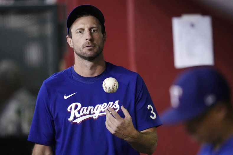 ARCHIVO - Foto del 22 de agosto del 2023, el pitcher de los Rangers de Texas Max Scherzer juega con una pelota en el dugout en la séptima entrada del juego ante los Diamondbacks de Arizona. El viernes 15 de diciembre del 2023, Scherzer se somete a una cirugía de espalda el jueves. (AP Foto/Ross D. Franklin, Archivo)