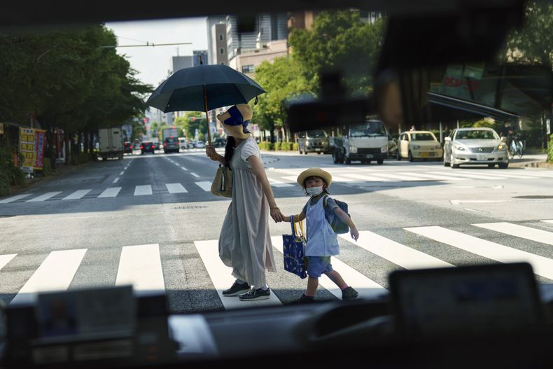 ARCHIVO - Una mujer cruza la calle con un niño, vista a través de la ventana de un taxi en Tokio el lunes 19 de julio de 2021. (AP Foto/David Goldman, Archivo)