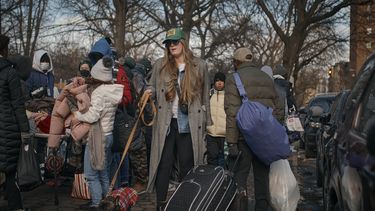 Una mujer pasea a su perro mientras migrantes recogen ropa distribuida por grupos de ayuda cerca del Centro de Asistencia al Migrante en la Escuela Primaria Santa Brígida, el sábado 20 de enero de 2024, en Nueva York. (AP Foto/Andres Kudacki)