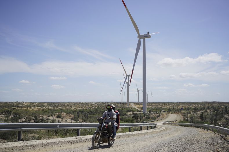 ARCHIVO - Dos personas en una motocicleta pasan cerca de unas turbinas eólicas en las afueras de Cabo de la Vela, Colombia, el 7 de febrero de 2025. (AP Foto/Ivan Valencia, Archivo)