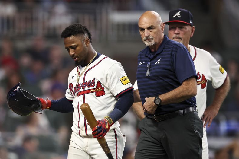 Ozzie Albies, izquierda, de los Bravos de Atlanta, abandona el partido de béisbol de Grandes Ligas acompañado del entrenador atlético George Poulis, derecha al frente, con una aparente lesión en la tercera entrada frente a los Nacionales de Washington, el lunes 22 de septiembre de 2025, en Atlanta. (AP Foto/Colin Hubbard)
