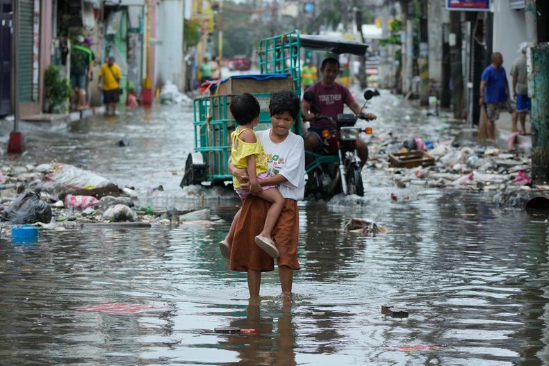 Una mujer y un niño cruzan una calle inundada por las tormentas del tifón Fung-wong y la marea alta el lunes 10 de noviembre de 2025 en Navotas, Filipinas. (AP Foto/Aaron Favila)