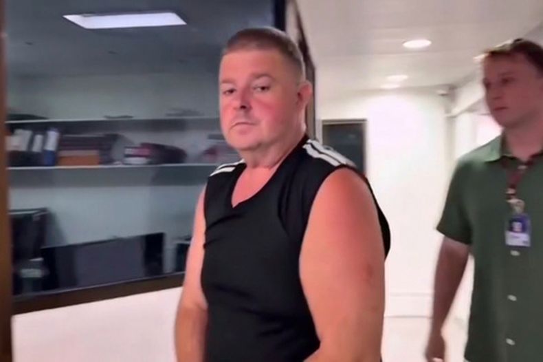 En esta imagen tomada de un video proporcionado por TPBS, el australiano identificado como Simon Peter Carman, a la izquierda, es escoltado en una comisaría en Pattaya, Tailandia, el domingo 28 de junio de 2026. (TPBS via AP)
