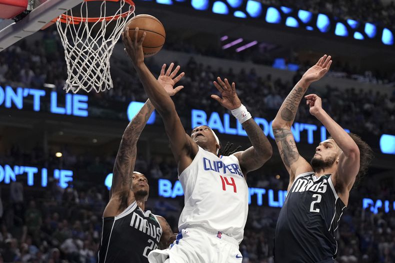 El base de los Clippers de Los Ángeles Terance Mann salta con el balón para anotar frente al alero P.J. Washington y el pívot Dereck Lively II de los Mavericks de Dallas en la serie de primera ronda de la postemporada el domingo 28 de abril del 2024. (AP Foto/Jeffrey McWhorter)
