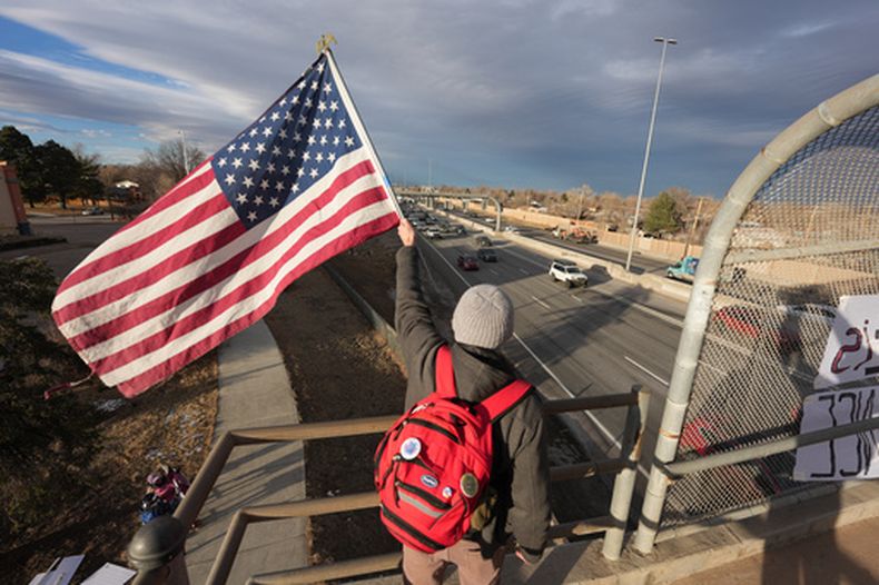 Un manifestante sostiene una bandera estadounidense mientras saluda a los automovilistas desde un paso elevado en la carretera Interestatal 25, el sábado 28 de enero de 2026, en Northglenn, Colorado. (AP Foto/David Zalubowski)