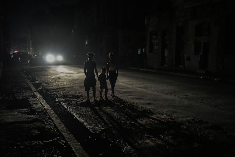 Varios residentes iluminados por las luces de un vehículo durante el apagón masivo en el que derivó la caída en el funcionamiento de una de las mayores plantas termoeléctricas del país, en La Habana, Cuba, el viernes 18 de octubre de 2024. (AP Foto/Ramón Espinosa)