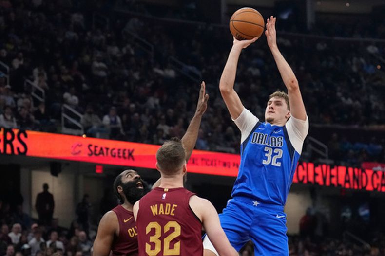 Cooper Flagg (32), de los Mavericks de Dallas, dispara sobre James Harden, izquierda, y Dean Wade (32), de los Cavaliers de Cleveland, durante la segunda mitad del juego de baloncesto de la NBA, el domingo 15 de marzo de 2026, en Cleveland. (AP Foto/Sue Ogrocki)