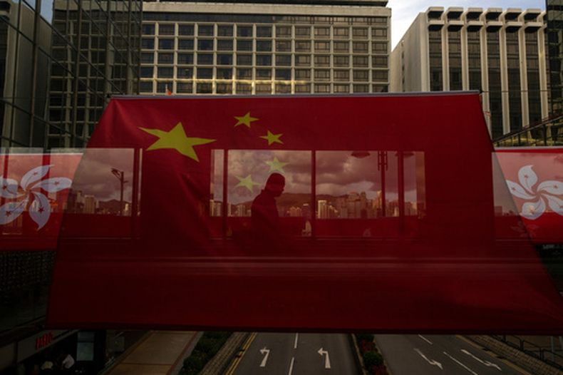 ARCHIVO - La silueta de un peatón en un paso peatonal se ve tras banderas chinas y de Hong Kong por el 26 aniversario de la entrega de la ciudad de Reino Unido a China, en Hong Kong, el 27 de junio de 2023. (AP Foto/Louise Delmotte, Archivo)