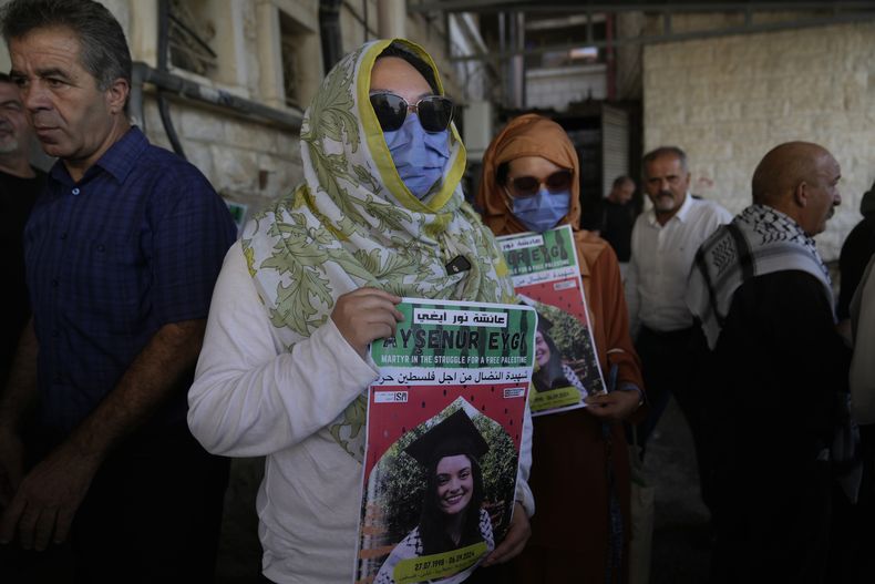 Dos compañeras activistas de Aysenur Ezgi Eygi, de 26 años, que según un testigo murió por disparos de soldados israelíes durante una protesta contra los asentamientos en Cisjordania, portan carteles con su nombre durante su funeral en la ciudad cisjordana de Nablus, el 9 de septiembre de 2024. (AP Foto/Nasser Nasser)