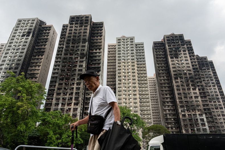 ARCHIVO - Una persona pasa ante torres residenciales destruidas por el fuego en el complejo de apartamentos Wang Fuk Court tras un incendio en noviembre, en el distrito de Tai Po de Hong Kong, el 20 de abril de 2026. (AP Foto/Chan Long Hei, Archivo)