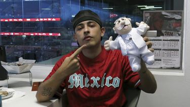 El rapero argentino Trueno posa con un muñeco de Dr. Simi después de lanzar la primera bola del partido entre los Diablos Rojos del México y el Águila de Veracruz en la Ciudad de México el jueves 2 de mayo de 2024.(Foto AP/Berenice Bautista)
