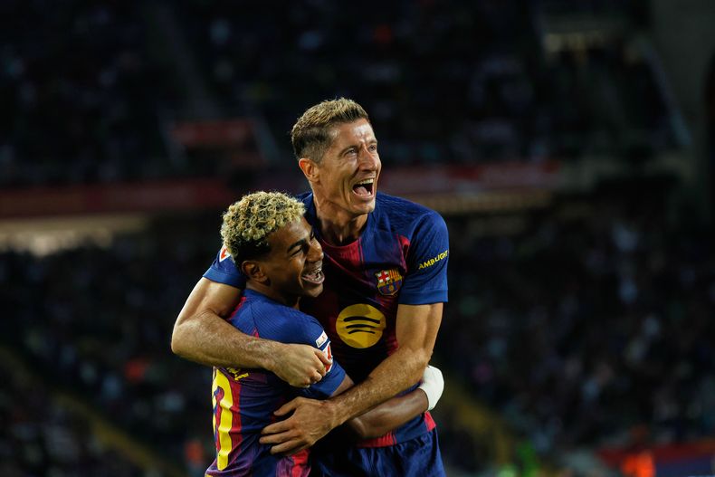 Robert Lewandowski, arriba, del Barcelona, celebra con Lamine Yamal el segundo gol de su equipo durante el partido de fútbol de la Liga Española entre el FC Barcelona y la Real Sociedad en el Estadio Olímpico Lluís Companys en Barcelona, España, el domingo 28 de septiembre de 2025. (AP Photo/Joan Monfort)