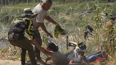 Una inmigrante que cruzó a Estados Unidos desde México es auxiliada a pasar debajo de alambre de púas en una de las márgenes del río Bravo, el jueves 21 de septiembre de 2023, en Eagle Pass, Texas. (AP Foto/Eric Gay)