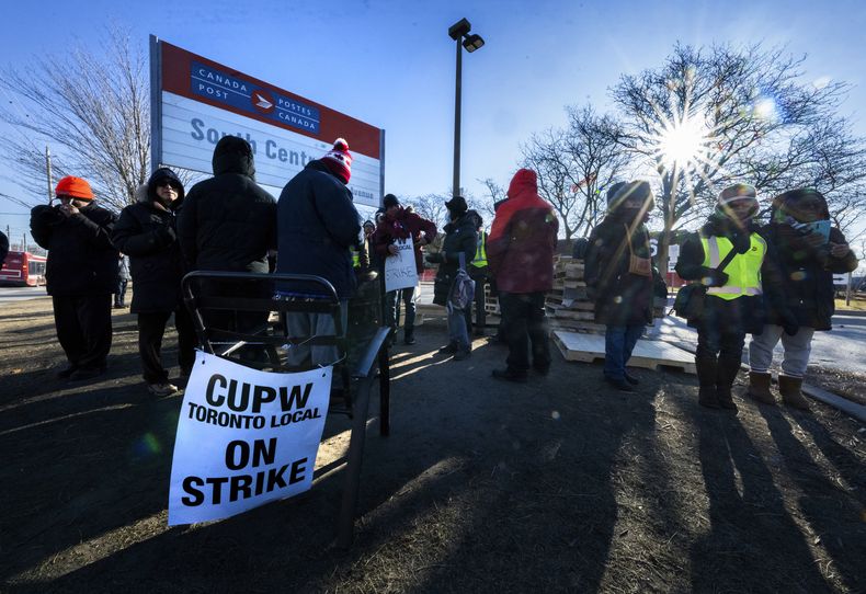 Empleados de Canada Post en huelga en Toronto escuchan en un altavoz la noticia de que el ministro de Trabajo, Steven MacKinnon, ha solicitado a la Junta de Relaciones Industriales de Canadá que ordene que los 50.000 empleados de la empresa regresen a sus puestos de trabajo, el viernes 13 de diciembre de 2024. (Frank Gunn /The Canadian Press vía AP)