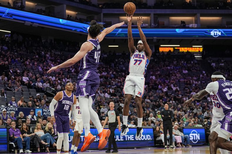 El base de los 76ers de Filadelfia, V.J. Edgecombe (77), lanza una canasta de tres puntos sobre el pívot de los Kings de Sacramento, Maxime Raynaud (42), durante la primera mitad de un juego de baloncesto de la NBA, el jueves 19 de marzo de 2026, en Sacramento, California. (Foto AP/Justine Willard)