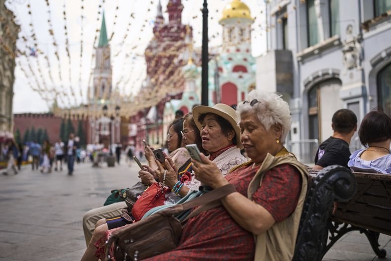 Un grupo de turistas, sentadas cerca del Kremlin, miran sus celulares, en Moscú, el 16 de julio de 2025. (AP Foto/Alexander Zemlianichenko)