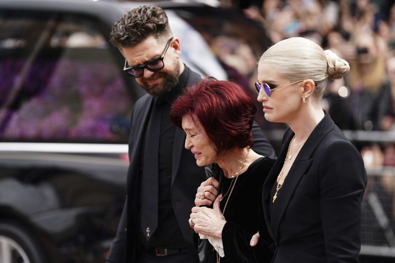 La familia de Ozzy Osbourne, de izquierda a derecha, Jack Osbourne, Sharon Osbourne y Kelly Osbourne, depositan flores y ven las flores colocadas en el banco del puente Black Sabbath en Broad Street en memoria del líder de Black Sabbath, Ozzy Osbourne, antes de la procesión fúnebre, en Birmingham, Inglaterra, el miércoles 30 de julio de 2025. (Jacob King/PA via AP)