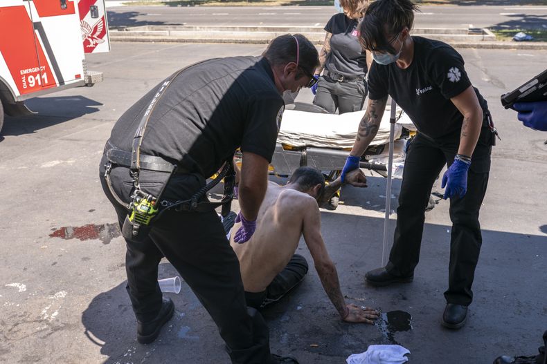 ARCHIVO - El capitán del departamento de bomberos de Salem, Matt Brozovich, a la izquierda, y el personal de ambulancias de Falck Northwest ayudan a atender a un hombre que experimenta un golpe de calor durante una ola de calor en Salem, Oregon, el 26 de junio de 2021. (AP Foto/Nathan Howard, Archivo)