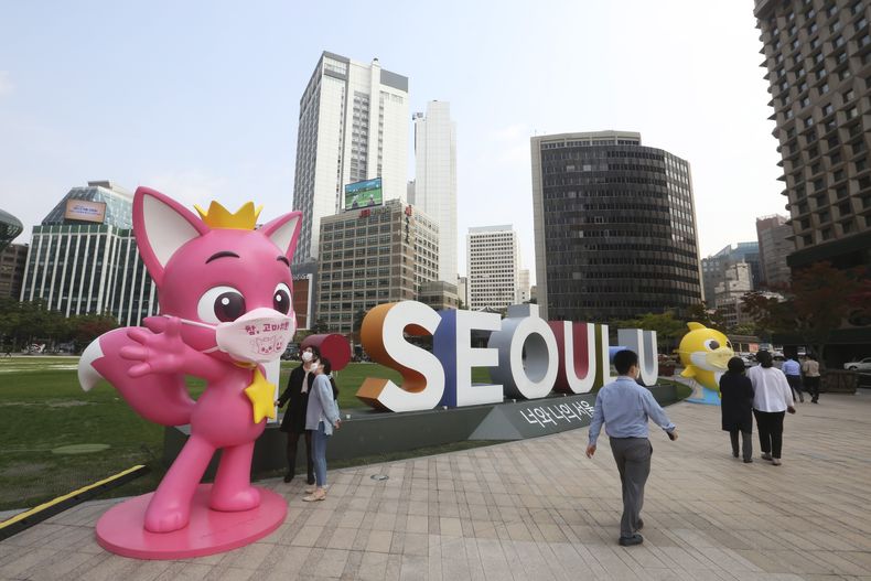 ARCHIVO - Varias personas pasan junto a personajes de Pinkfong, una empresa surcoreana de contenido para niños, durante una campaña de prevención del COVID-19 en la Plaza del Ayuntamiento en Seúl, el 12 de octubre de 2020. En la mascarilla del personaje pone Muchas gracias. (AP Foto/Ahn Young-joon, archivo)