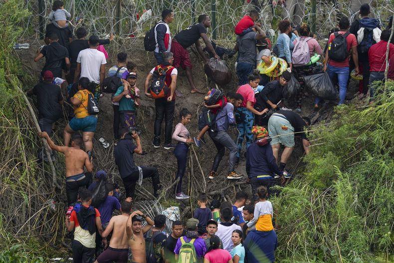 Migrantes avanzan sobre una de las márgenes del río Bravo (Rio Grande, en inglés) mientras miembros de la Guardia Nacional de Texas les impiden el paso detrás de hileras de alambre de púas, el jueves 11 de mayo de 2023, en esta fotografía tomada desde Matamoros, México. Las restricciones al asilo relacionadas con la pandemia de COVID-19, conocidas como Título 42, iban a expirar el 11 de mayo. (AP Foto/Fernando Llano)