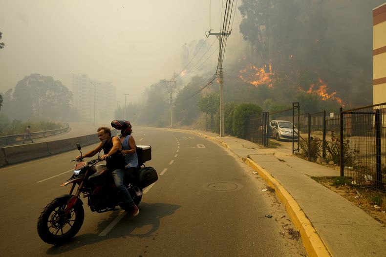 ARCHIVO - Residentes evacúan en una motocicleta entre incendios forestales en Viña del Mar, Chile, el 3 de febrero de 2024. Los científicos dicen que el cambio climático crea condiciones que hacen más probables la sequía y los incendios forestales que afectan ahora a Sudamérica. (AP Foto/Esteban Felix, Archivo)