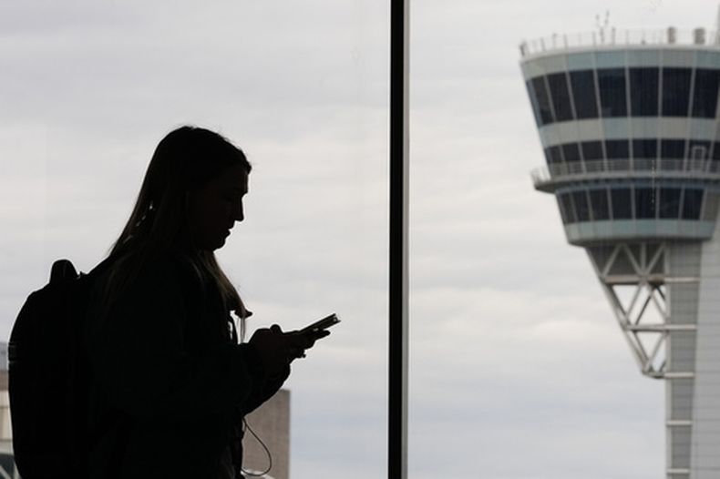 ARCHIVO – Una viajera con un teléfono inteligente camina frente a una torre de control de tráfico aéreo en el Aeropuerto Internacional de Filadelfia, en Filadelfia, el 27 de marzo de 2026. (AP Foto/Matt Rourke, Archivo)
