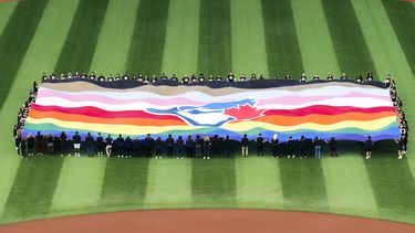 Un grupo de personas sostiene una bandera de los Azulejos de Toronto para festejar el Fin de Semana del Orgullo, antes del juego ante los Mellizos de Minnesota, el viernes 9 de junio de 2023 (Mark Blinch)