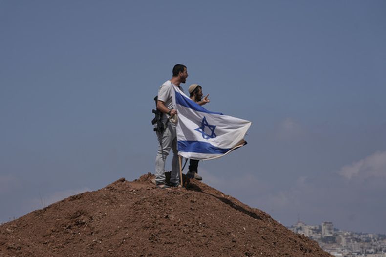 Colonos israelíes colocan una bandera israelí sobre una colina después de que fuera retirada por activistas de paz israelíes y extranjero durante una protesta en apoyo de propietarios locales de terrenos cuyas propiedades se ven amenazadas de ser ocupadas por colonos, a las afueras de la ciudad cisjordana de Beit Sahour, el viernes 14 de agosto de 2026. (AP Foto/Mahmoud Illean)