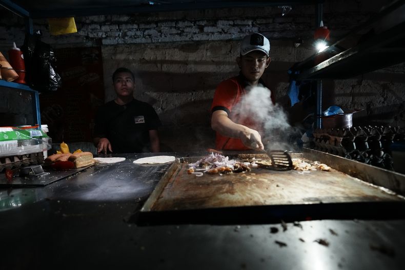 ARCHIVO - Un vendedor ambulante prepara comida iluminado por una bombilla alimentada por un generador en medio de apagones, el lunes 23 de septiembre de 2024, en Manta, Ecuador. (AP Foto/Dolores Ochoa, Archivo)
