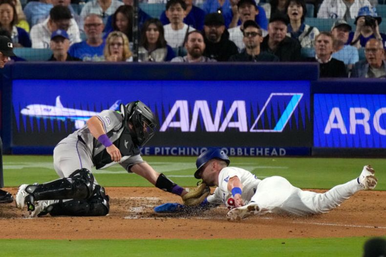 Dalton Rushing (derecha), de los Dodgers de Los Ángeles, es puesto fuera (tagged out) por el receptor de los Rockies de Colorado, Braxton Fulford, mientras intenta anotar tras un toque de bola de jugada de selección de Miguel Rojas durante la quinta entrada de un partido de béisbol, el martes 7 de julio de 2026, en Los Ángeles. (Foto AP/Mark J. Terrill)