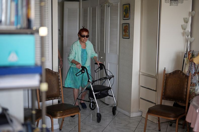 Anna Fischbein, de 86 años, camina en su apartamento durante una entrevista sobre la pérdida de una amada trabajadora haitiana de atención domiciliaria cuyo estatus de protección temporal (TPS, por sus siglas en inglés) expiró esta semana, el jueves 30 de julio de 2026, en Sunny Isles Beach. (AP Foto/Rebecca Blackwell).